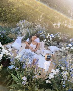 a man and woman sitting on the ground surrounded by flowers