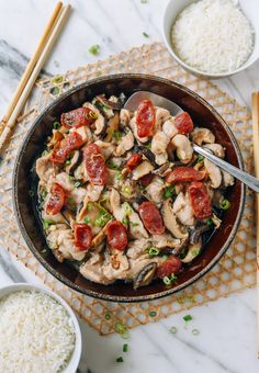 a skillet filled with chicken, tomatoes and rice next to chopsticks on a table