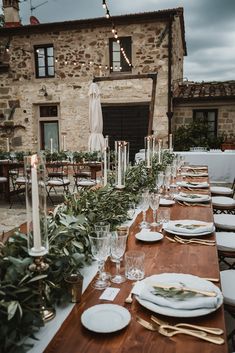 an outdoor dining table set with place settings and greenery on the tables for dinner