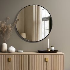 a large round mirror on the wall above a dresser with vases and other items