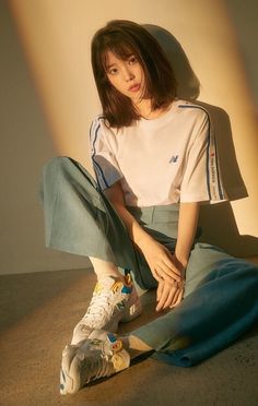 a woman sitting on the ground with her legs crossed, wearing adidas sneakers and a white t - shirt