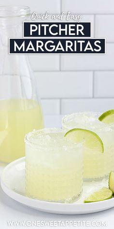 two glasses filled with lemonade and limes on a white plate next to a pitcher