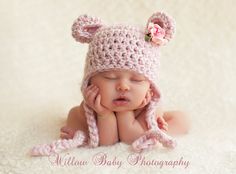 a newborn baby wearing a pink crocheted bear hat and holding her hands to her face