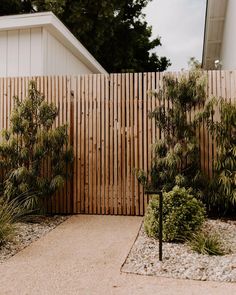 a wooden fence next to a house with trees and bushes in front of the fence