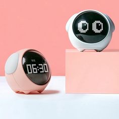 two alarm clocks sitting next to each other on top of a pink blocky surface