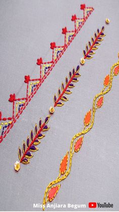 three embroidered designs with gold and red trimmings on a gray surface, one is in the middle