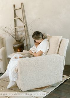 a woman sitting in a chair with a blanket on her lap and reading a book