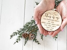 two hands holding a christmas ornament with pine cones and greenery in the background