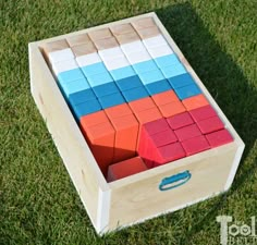 a wooden box filled with colorful blocks on top of green grass next to a blue and red object