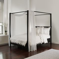 a four poster bed with white linens and pillows in a room that has hardwood floors