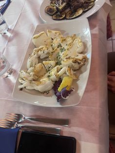 a table topped with plates of food next to wine glasses and utensils on top of a white table cloth