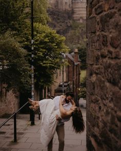 a man and woman dancing on the sidewalk in an alleyway with stone buildings behind them