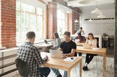 people sitting at desks working on laptops in an open room with large windows