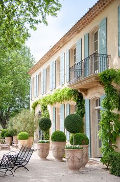 an outdoor patio with potted plants and chairs in front of a large building that has blue shutters