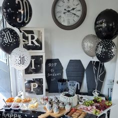 a table topped with lots of food and balloons next to a clock on the wall