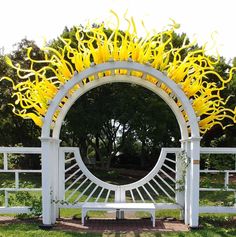 a white bench sitting under a yellow sunflower sculpture