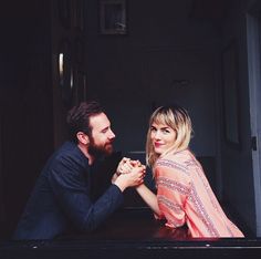 a man and woman sitting at a table with one holding the other's hand