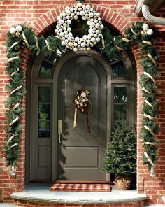 a christmas wreath on the front door of a brick house with evergreens and pine cones