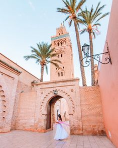 a woman in a white dress is walking through an archway with palm trees behind her