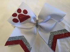 The Paw Print Design Cheer Bows is handmade with the finest materials for it to last all cheer season long. It is available in a variety of color combinations. This model comes with a black pony attached. This bow measures 7 inches, which is the standard bow size for cheerleading bows. Ready to be in the spotlight? Our cheer bows will make your squad dazzle. This bow comes in different colors. If you don´t find what you are looking for, request a custom order. Check out all of our cheer bows, ma Cheer Squad Gifts, Cute Cheer Bows, Softball Accessories, Cheer Season, Cheer Captain, Cheer Hair Bows, Softball Bows, Glitter Cheer Bow, Cheer Uniforms