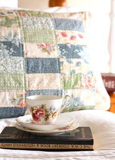 a stack of books sitting on top of a bed next to a cup and saucer