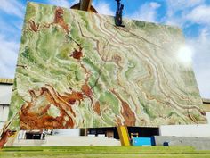 a large green and brown marble sculpture in front of a building with a sky background