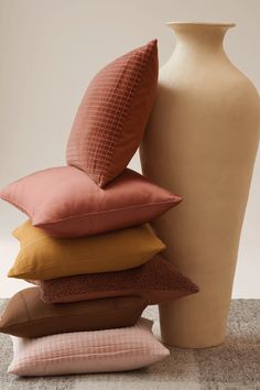 a stack of pillows sitting next to a vase on top of a carpeted floor