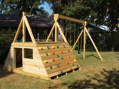 a wooden play structure with swings and climbing bars in the back yard, next to a tree