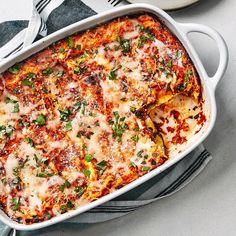 a casserole dish with cheese and vegetables in it on a table next to silverware