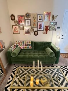 a living room with green couches and pictures on the wall above it, candles in front of a glass coffee table