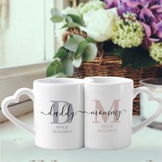 two coffee mugs sitting on top of a counter next to a basket with flowers