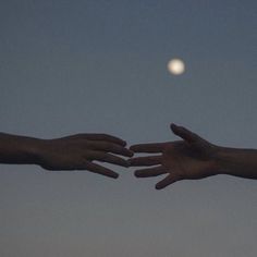 two hands reaching out towards each other with the moon in the background