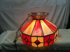 a stained glass lamp is sitting on top of a white cloth covered tablecloth with a chain hanging from it