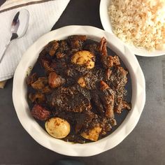 two bowls filled with meat and rice on top of a black tablecloth next to spoons