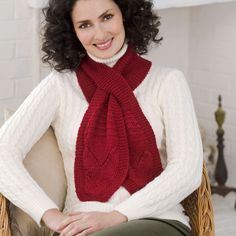 a woman sitting in a chair wearing a red knitted scarf and smiling at the camera