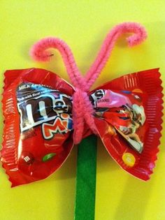 a candy bar shaped like a butterfly sitting on top of a green stick and wrapped in pink paper