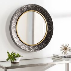 a round mirror on the wall above a table with a potted plant next to it