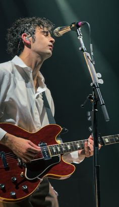 a man holding a guitar while standing in front of a microphone