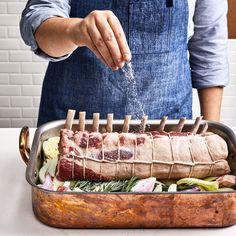 a person sprinkling seasoning onto a rack of meat in a roaster