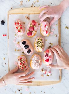 hands reaching for doughnuts on a tray with sprinkles and toppings