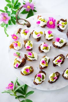 small appetizers are arranged on a white plate with pink flowers and green leaves