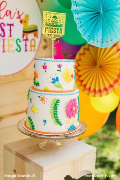 a colorful birthday cake sitting on top of a wooden table in front of paper fans