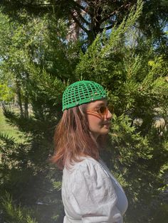 a woman wearing sunglasses and a green hat standing in front of some trees with her hands on her hips