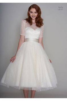 a woman wearing a white dress with polka dots on the waist and sleeves, standing in front of a gray background