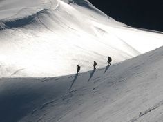 three people walking up the side of a snow covered mountain