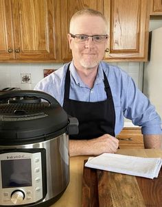 a man sitting at a kitchen counter in front of an electric pressure cooker with the lid open