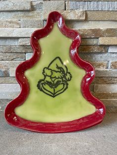 a red and green ceramic christmas tree dish on a stone wall with a brick background