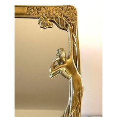 a gold colored mirror with a woman holding a vase in it's hand and the reflection of a tree behind it