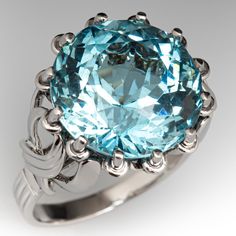 This bright cocktail ring is centered with a round modified brilliant cut aquamarine, weighing 11.94 carats, in a twelve-prong setting. The shoulders are each accented with a figure-eight detail. The ring measures 17.5mm at the top, rises 11.7mm above the finger, tapering to 2.4mm wide and 0.7mm thick at the base of the shank. Currently, the platinum ring fits a size 6.75. Formal Light Blue Topaz Ring, Luxury Turquoise Topaz Ring For Formal Occasions, Luxury Formal Turquoise Topaz Ring, Round Art Deco Topaz Ring For Formal Occasions, Formal Round Topaz Ring In Art Deco Style, Formal Art Deco Round Topaz Ring, Whimsical Rings, Whimsical Ring, Teal Jewelry