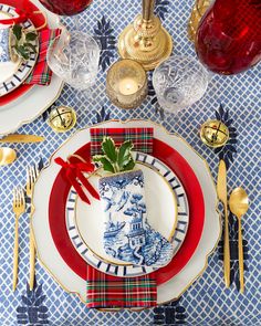 the table is set for christmas dinner with red and white plates, silverware, and gold place settings